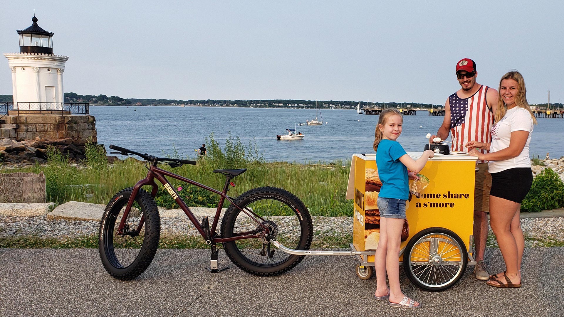 Family roasting s'mores from the back of a mountain bike by the water