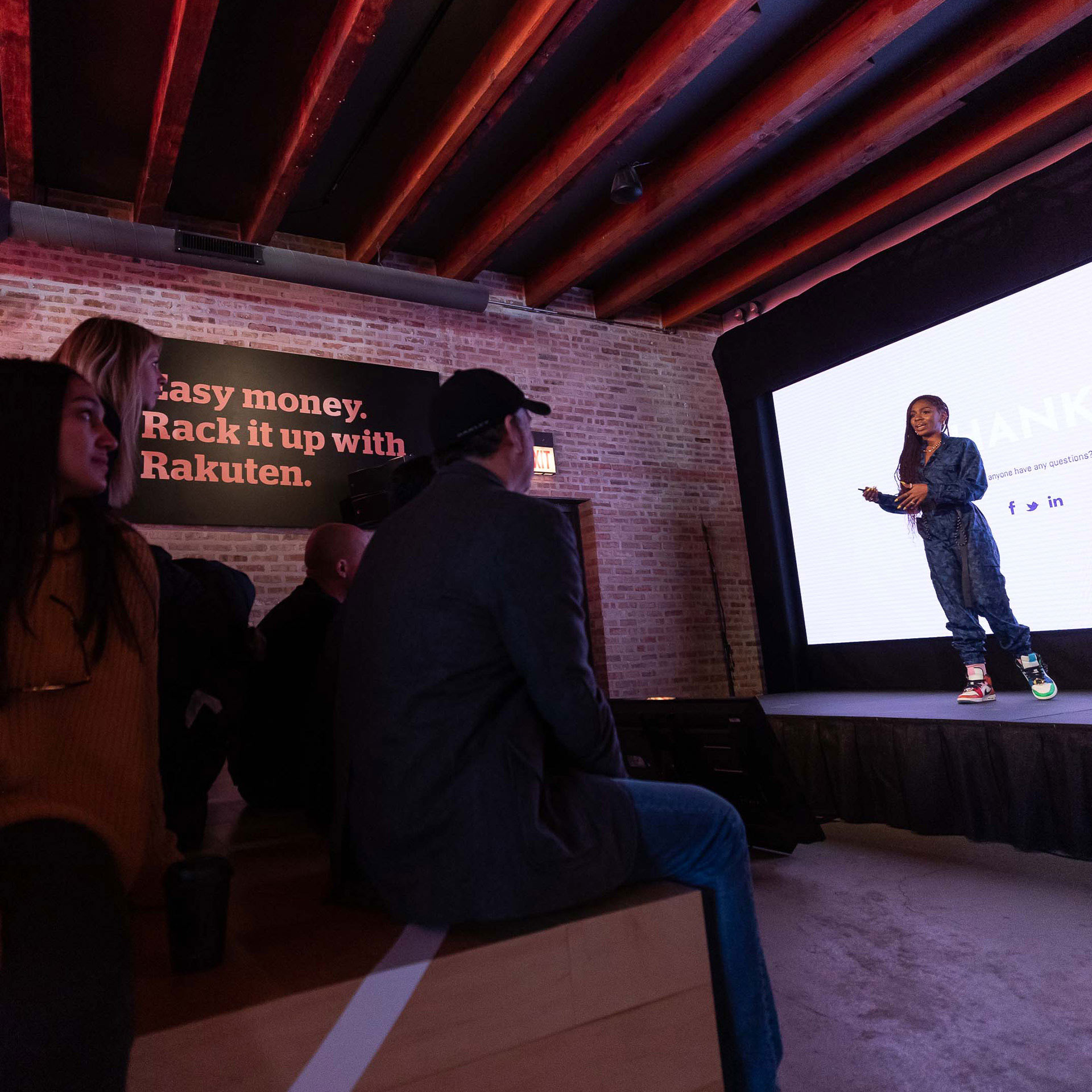 A speaker with colorful shoes looks out at the audience and explains Rakuten House 